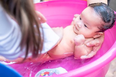 Asyalı anne temizlik yapmak için bebeğe duş aldırıyor. Temizlik için çocuğu banyoya koyuyor. Anne ve çocuk arasındaki aile arasında bebek kremi ürünleri için kullanılıyor.