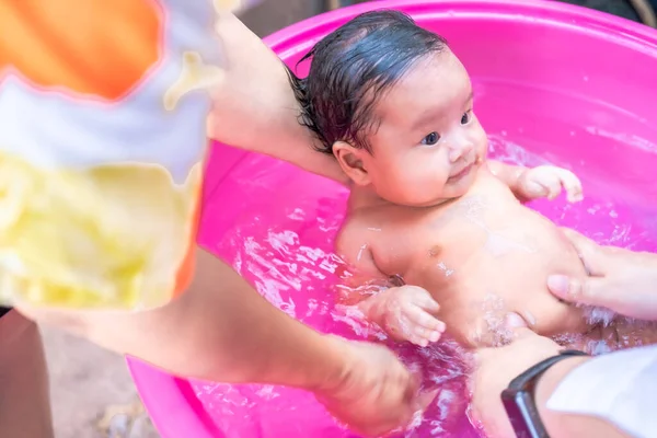 Asyalı anne temizlik yapmak için bebeğe duş aldırıyor. Temizlik için çocuğu banyoya koyuyor. Anne ve çocuk arasındaki aile arasında bebek kremi ürünleri için kullanılıyor.