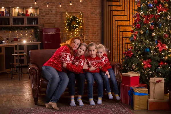 幸せな若い母親と彼女の娘たちは クリスマス イブに装飾されたクリスマスツリーを持つ居心地の良い暗いリビングルームでソファに座っている間 しっかりと抱きつく 家族と冬の夜 — ストック写真