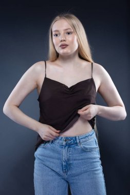 Kot pantolonlu genç sarışın kadın ve koyu gri arka planda kahverengi atlet.