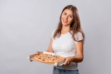 Beyaz tişörtlü bir kız beyaz arka planda izole bir şekilde elinde sıcak pizza kutusuyla poz veriyor. Yemek siparişi alan bir müşteri konsepti..