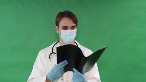 首の周りに聴診器付きの白いコートを着た医師が 緑の背景に隔離された医療記録を持つ黒いフォルダを通って出ています キーのための緑の画面のクロマキーの背景 — ストック動画