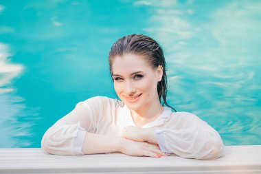 Havuzun kenarında göğsüne kadar suya batmış beyaz gömlekli, ıslak saçlı güzel bir kızın portresi..