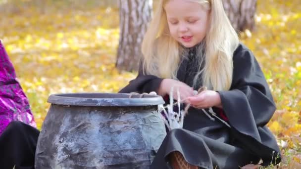 一个穿着黑色斗篷的小女孩从秋日公园背靠着的绞刑架上的大锅玩具骷髅里取出来 儿童的光环 — 图库视频影像