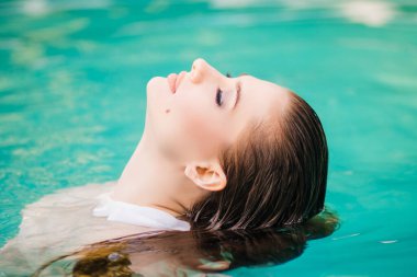 Havuzda göğsüne kadar duran beyaz gömlekli, ıslak saçlı güzel bir kızın portresi..