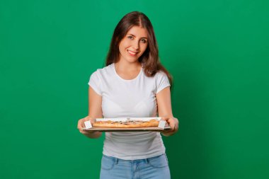 Beyaz tişörtlü bir kadın yeşil arka planda izole bir şekilde elinde sıcak pizza kutusuyla poz veriyor. Modelleme. Yemek siparişi alan bir müşteri konsepti.. 