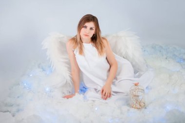 Beyaz ceketli, arkasında büyük beyaz kanatları olan çekici bir kız beyaz bulutlarda otururken poz veriyor..