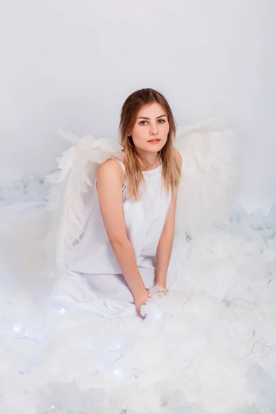 一个穿着白色紧身衣 背着白色大翅膀的漂亮姑娘坐在白云中摆姿势 — 图库照片
