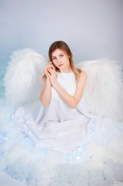 Beyaz ceketli, arkasında büyük beyaz kanatları olan çekici bir kız beyaz bulutlarda otururken poz veriyor..