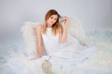 Beyaz ceketli, arkasında büyük beyaz kanatları olan çekici bir kız beyaz bulutlarda otururken poz veriyor..