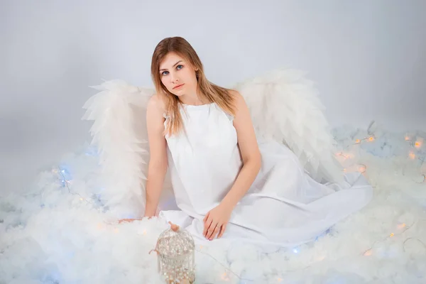 一个穿着白色紧身衣 背着白色大翅膀的漂亮姑娘坐在白云中摆姿势 — 图库照片