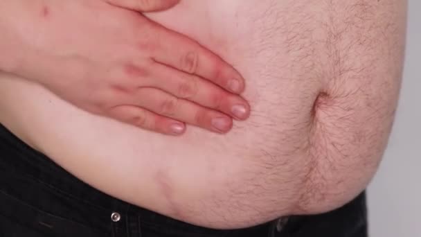 胖子慢吞吞地拍打着他的手 拍拍他那光秃秃的大肚子 脂肪的褶皱在抖动 被白色的背景隔离了男性腹部紧闭 — 图库视频影像