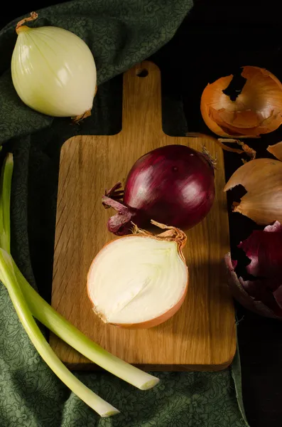 Mängd lök på en skärbräda med skalet och mörk grön — Stockfoto