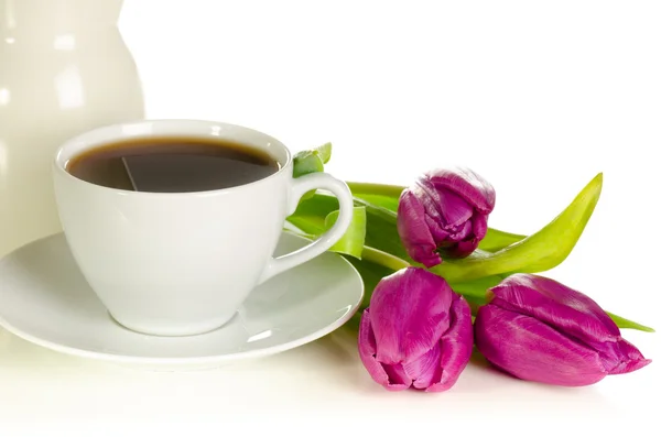 White cup of coffee with bunch of purple tulips on white backgro — Stock Photo, Image