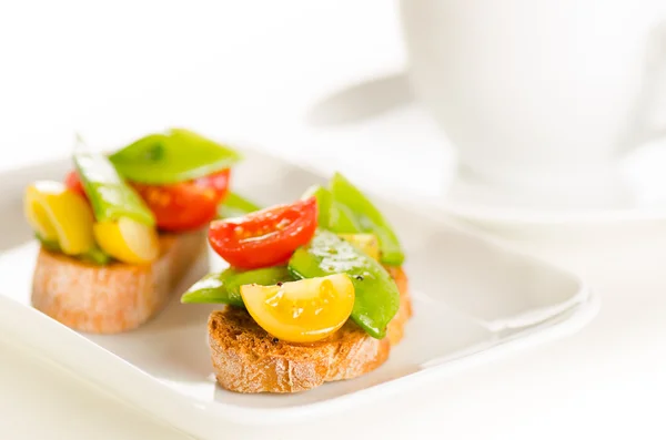 Cherry tomatoes and snow peas crostini with tea — Stock Photo, Image