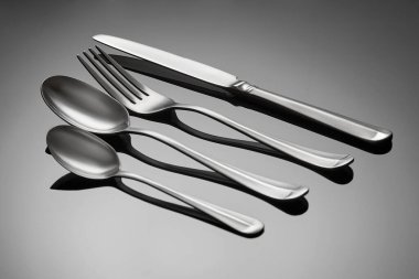 Çatal bıçak takımı - çay kaşığı, masa kaşığı, çatal ve bıçak. Çatal bıçak takımı gri parlak bir arka planda yatıyor. Çatal bıçak takımı çapraz dizilmiş..