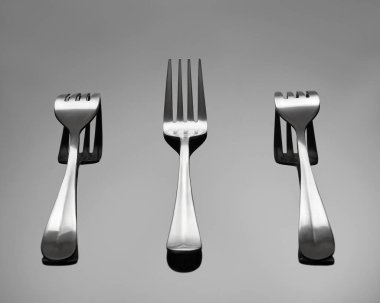 Çatallar gri parlak bir arka planda yatıyor. Orta çatal dişleri yukarıda yatar, çatallar yan tarafta dişleri aşağıda yatar.