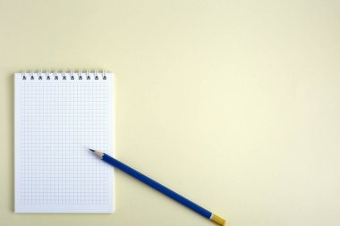 Sarı arka planda not defteri. Defterde bir kurşun kalem var. Eşyalar sol alt köşede yer alıyor. Yukarıdan bak, düz yat