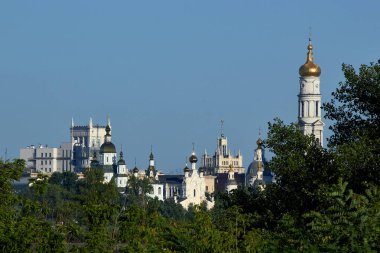 Mavi gökyüzüne karşı birkaç kilisenin kubbeleri. Ön planda ağaçlar ve çalılar