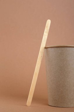 Tek kullanımlık kağıt bardak ve kahverengi arka planda tahta kahve çubuğu.