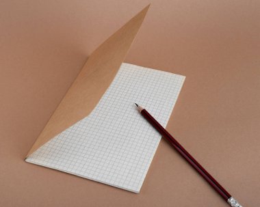 Kahverengi arka planda boş not defteri ve kalem. Markan için boş yer
