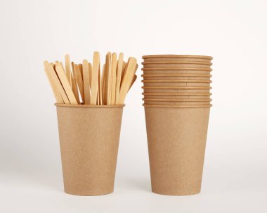 Tek kullanımlık kağıt bardaklar ve beyaz arka planda ahşap kahve çubukları. Markan için boş yer