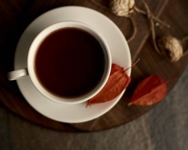 Tahta üzerinde çay olan bir fincan. Bardağın yanında kurumuş çiçekler var. Düz yatıyordu. Sığ alan derinliği