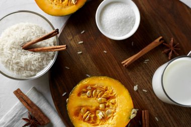 Tahtada balkabağını kes. Balkabağının yanında pirinç ezmesi, süt, şeker, tarçın çubukları ve anason var. Sütlü pirinç lapası ve balkabağı. Seçici odaklanma. Düz yatıyordu