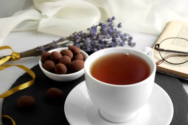 Gri tahtada bir fincan çay ve şeker. Tahtanın arkasında bir demet lavanta, bir kitap ve gözlük var. Yıl Rengi 2022 Çok Peri