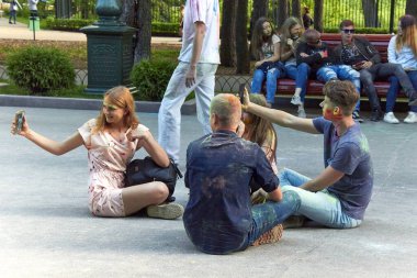 Kharkiv, Ukrayna, 19 Mayıs 2018 Holi renk festivali. Gençler ara sokağın ortasında oturup akıllı telefonlardan selfie çekiyorlar. Çok renkli boyalı insanların yüzleri ve kıyafetleri.