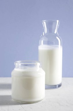 Yoğurt, kefir ya da bardakta mayalanmış süt ürünü ve beyaz bir masada şişe. Beyaz leylak arka planı. Sağlıklı gıda konsepti