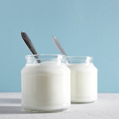 Yoğurt, kefir ya da beyaz bir masada cam kavanozlarda mayalanmış süt ürünü. Beyaz ve mavi arka plan. Sağlıklı gıda konsepti
