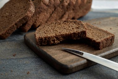 Bir parça çavdar ekmeği tahta bir tahtanın üzerinde iki parçaya bölündü. Arka planda dilimlenmiş çavdar ekmeği