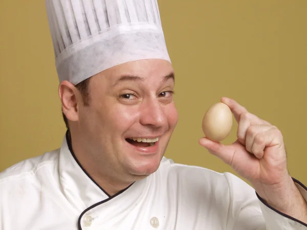 Νεαρός σεφ κρατώντας ένα φρέσκο αυγό σε κίτρινο φόντο. — Φωτογραφία Αρχείου