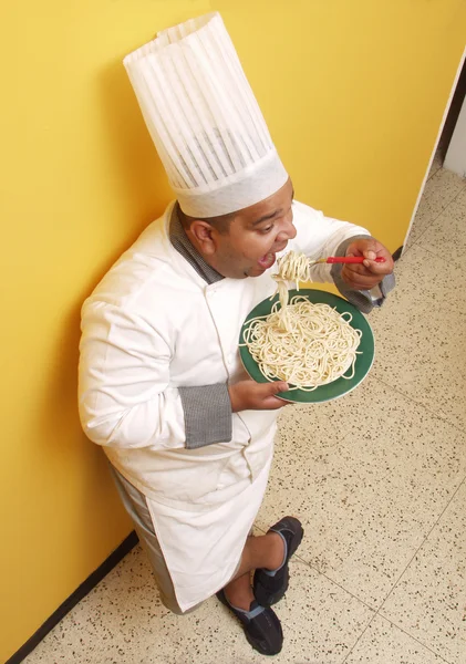 Koch isst Pasta in einer Küche. — Stockfoto