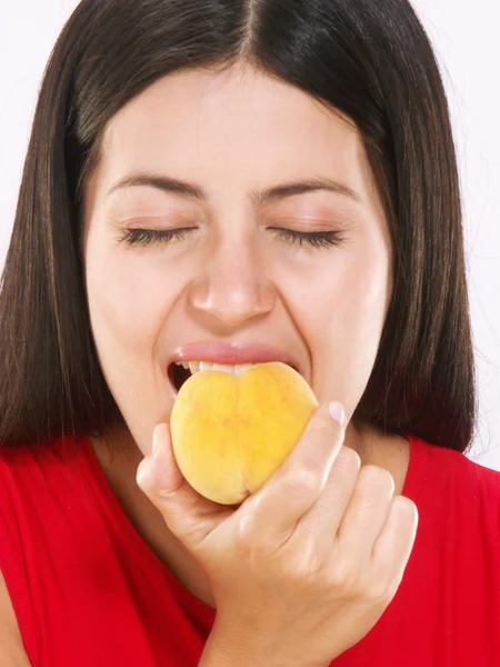 Jonge vrouw eten een perzik op witte achtergrond — Stockfoto