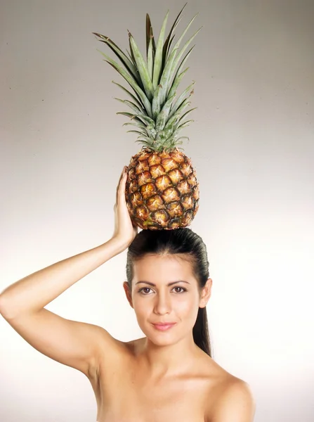 Young woman holding a pineapple over her head on white background — Stock Photo, Image