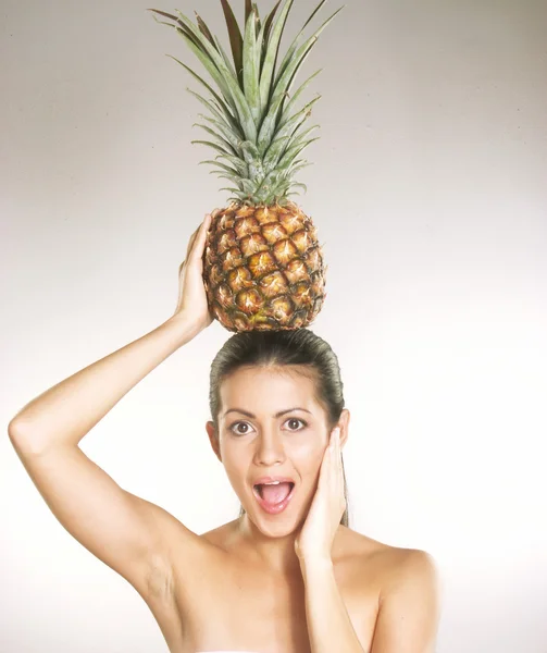 Ung kvinna med en ananas över huvudet på vit bakgrund — Stockfoto