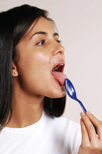 Jovem mulher lambendo uma colher de plástico — Fotografia de Stock