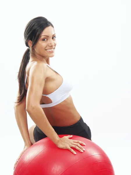 Ung kvinna gör fitness motion med en röd boll. — Stockfoto