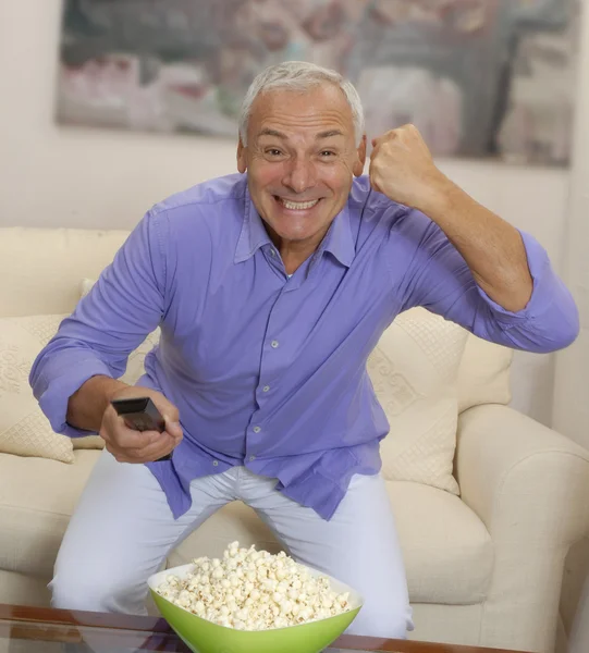 Senior man televisie kijken en eten popcorn. — Stockfoto