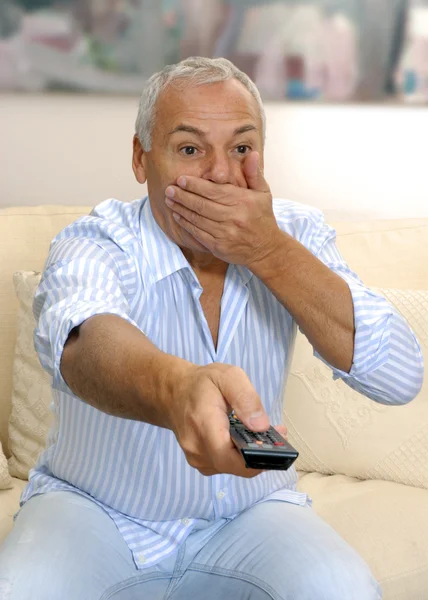 Homme âgé regardant la télévision et tenant une télécommande . — Photo