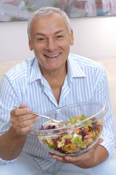 Happy senior mannen äter färska grönsaker sallad hemma. — Stockfoto