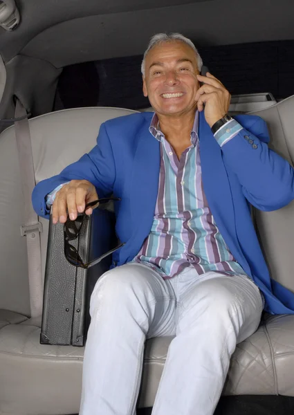 Starszy bogacz za pomocą telefonów komórkowych wewnątrz samochodu. — Zdjęcie stockowe