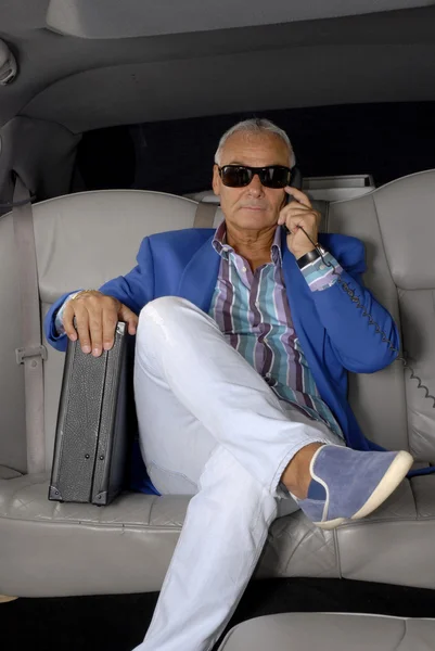 Business senior man on phone inside a car holding a suitcase. — Stock Photo, Image