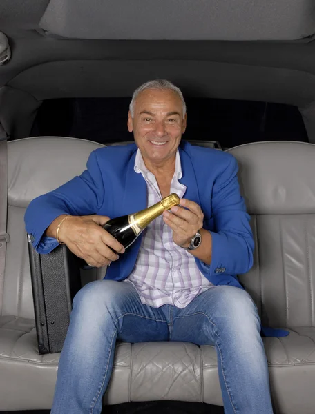 Happy senior man drinking champagne inside a limousine. — Stock Photo, Image