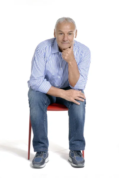 Portrait of a casual senior sitting on a red chair on white background. — Stock Photo, Image