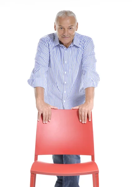 Senior man holding a red chair on white background. — Stock Photo, Image