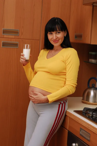 Mujer embarazada joven bebiendo leche en una cocina — Foto de Stock