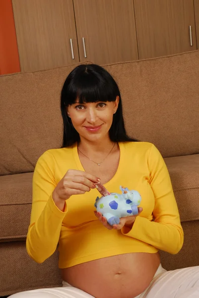 Jonge en gelukkig zwangere vrouw met een piggy bank — Stockfoto